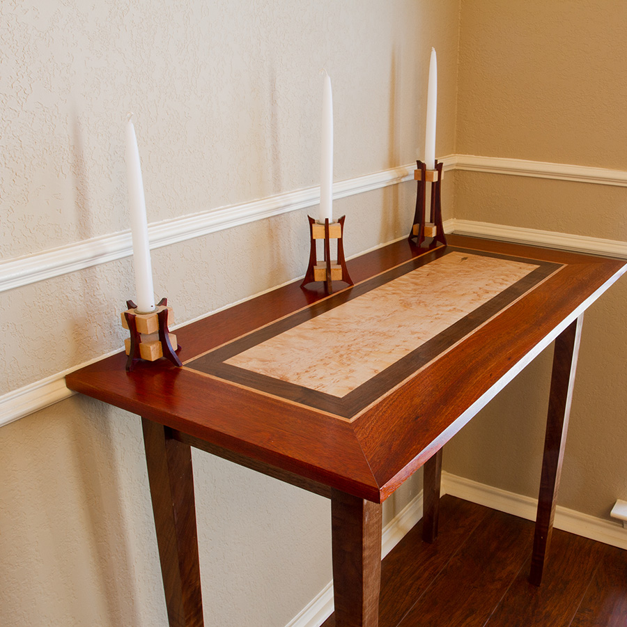 Table used as sideboard. Has various colors of wood inlaid. Also, holds three candlesticks.